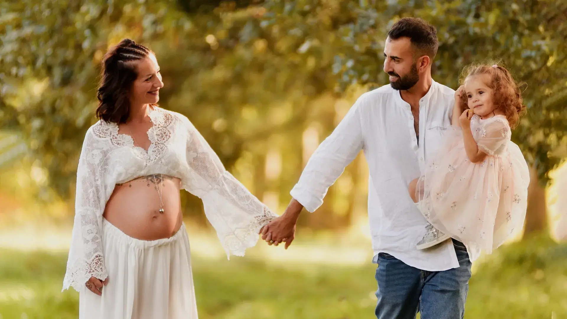 Servizio fotografico di gravidanza all'aperto con futura mamma, papà e figlia durante una passeggiata in un parco a Torino