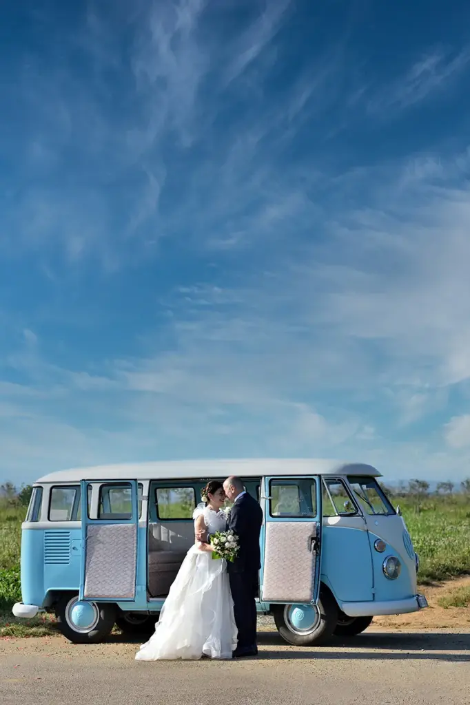 Sposi abbracciati davanti a un Volkswagen T1 azzurro durante un servizio fotografico di matrimonio all'aperto.