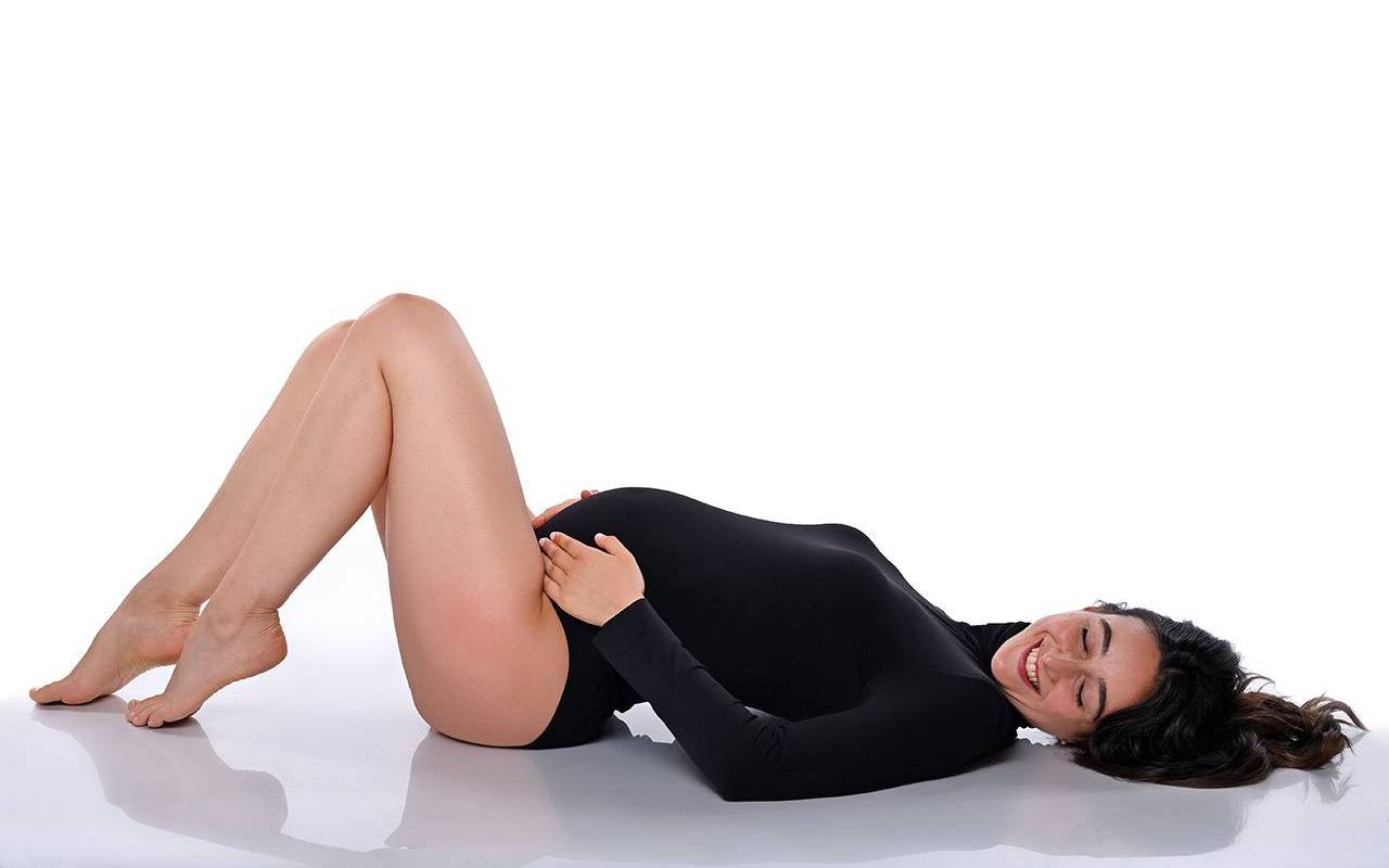Donna in gravidanza distesa con body nero su sfondo chiaro