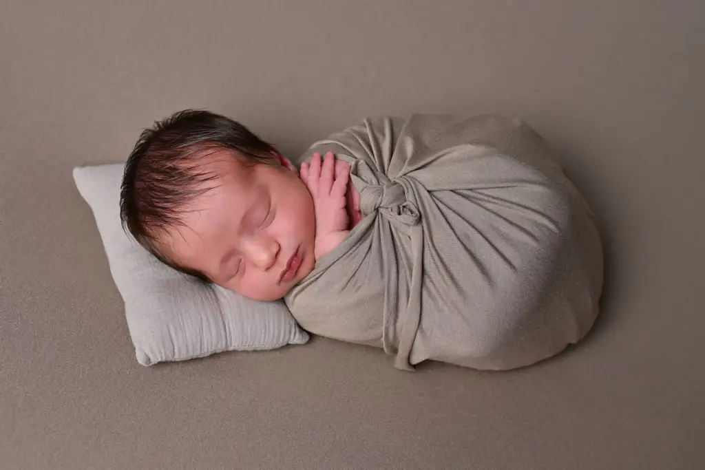 Neonato addormentato avvolto in un morbido tessuto durante un servizio fotografico newborn