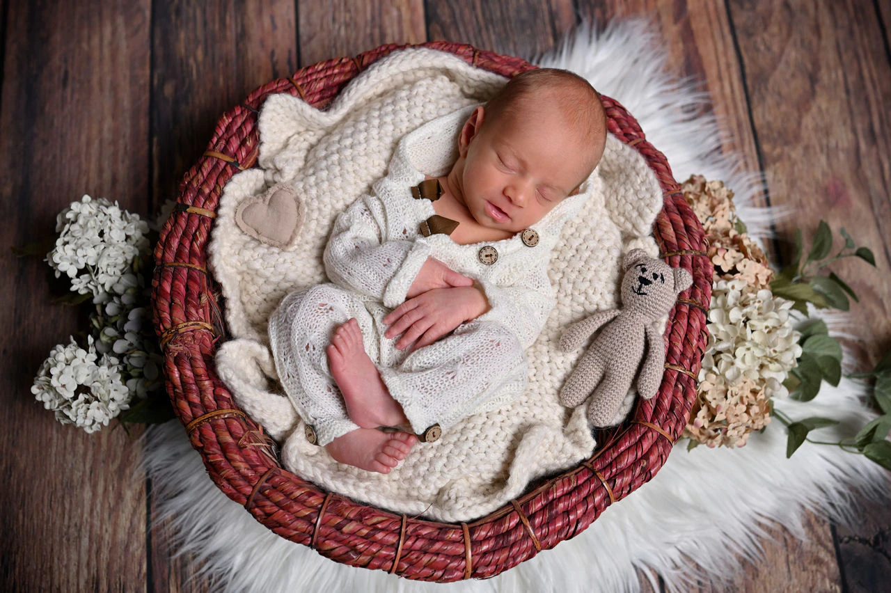 Neonato addormentato in un cesto con coperta e decorazioni floreali