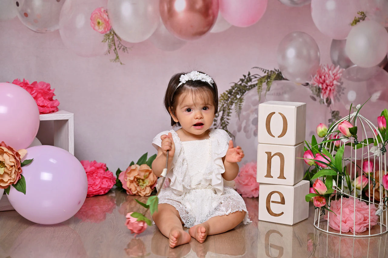 Bambina nella scenografia rosa con fiori e palloncini per il primo compleanno