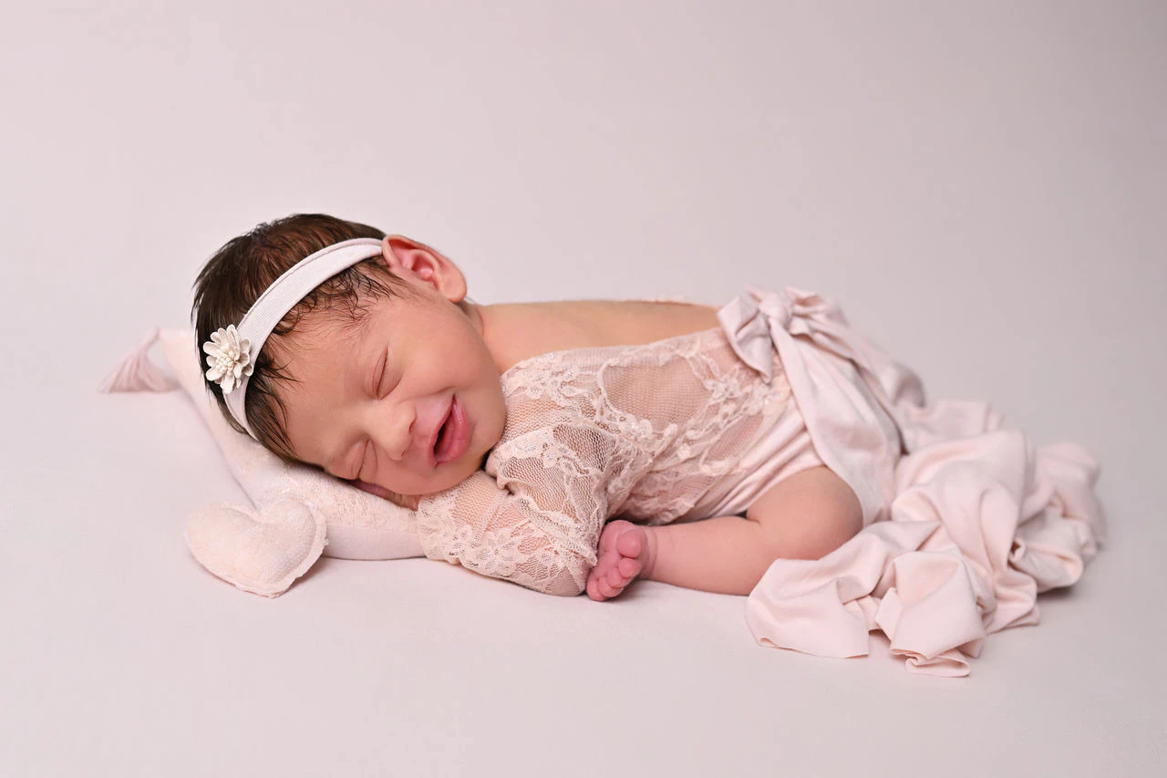 Neonato addormentato su tessuto rosa durante una sessione fotografica newborn