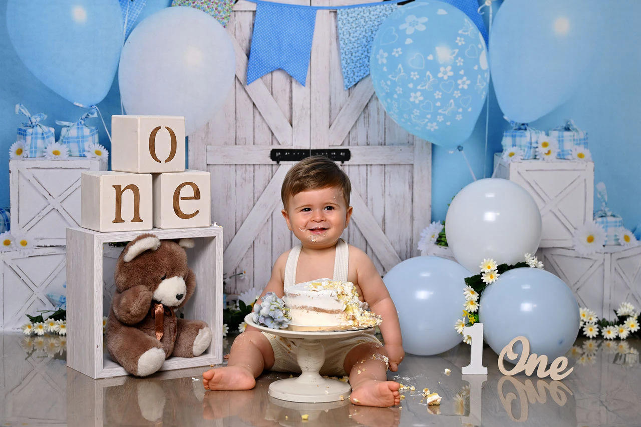Bambino sorridente davanti alla torta nella scenografia azzurra del primo compleanno