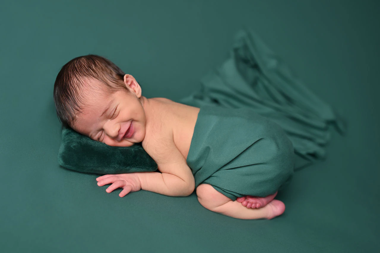 Neonato addormentato avvolto in un tessuto verde durante il servizio fotografico
