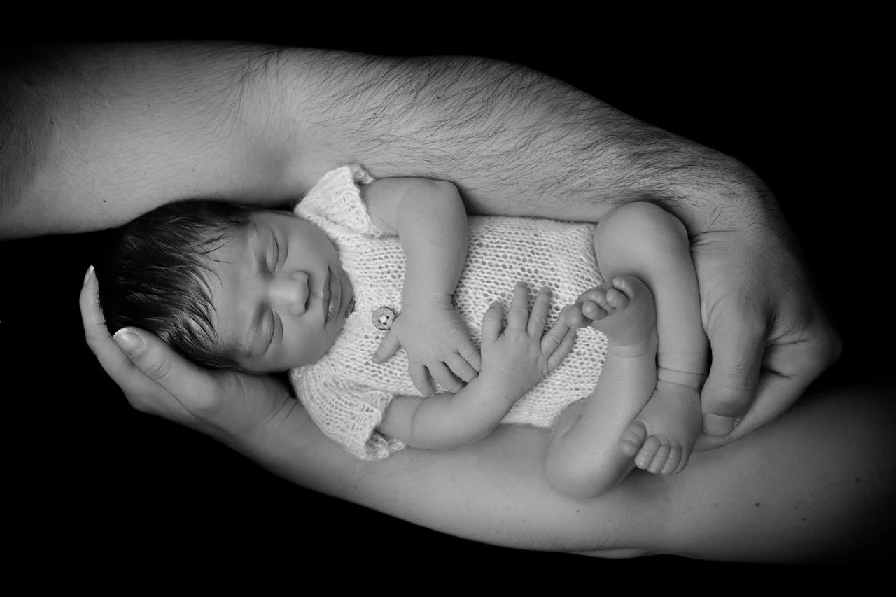 Neonato tra le mani dei genitori fotografato in bianco e nero