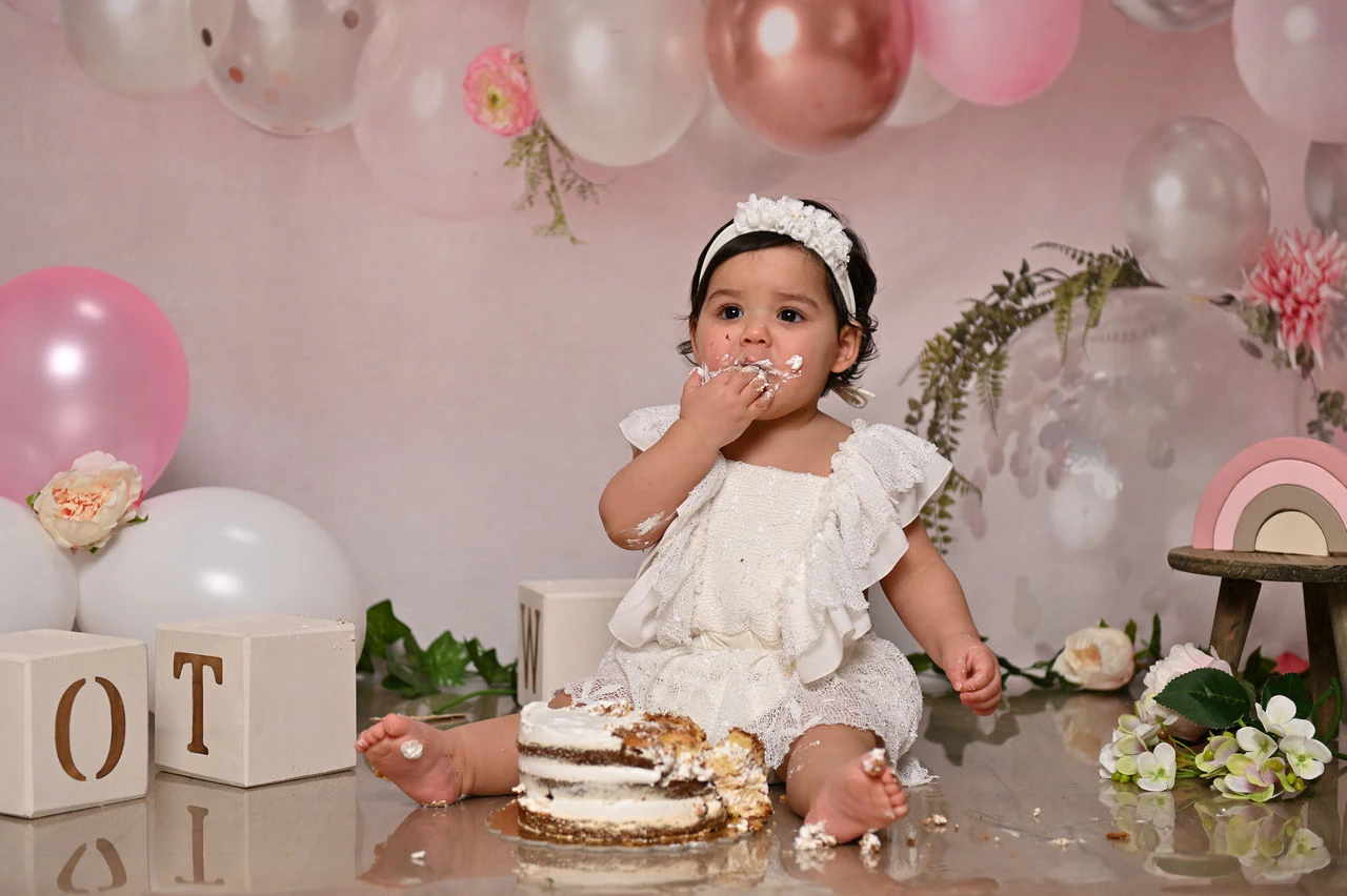 Bambina con torta nella scenografia rosa durante il servizio fotografico Smash Cake